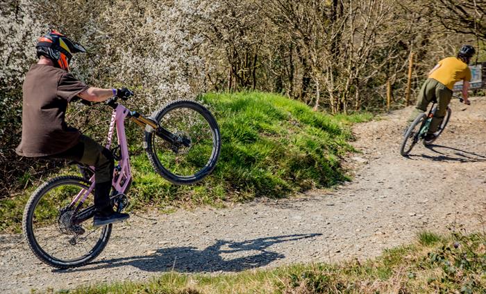 Two riders having fun in the sun, one is pulling a wheelie.